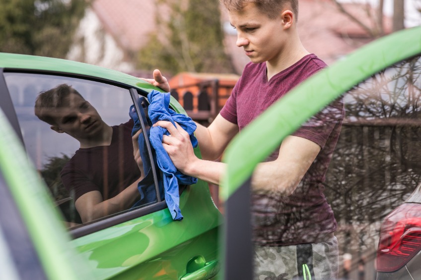 Teenage boy washing a green car with a blue rag for a school fundraiser